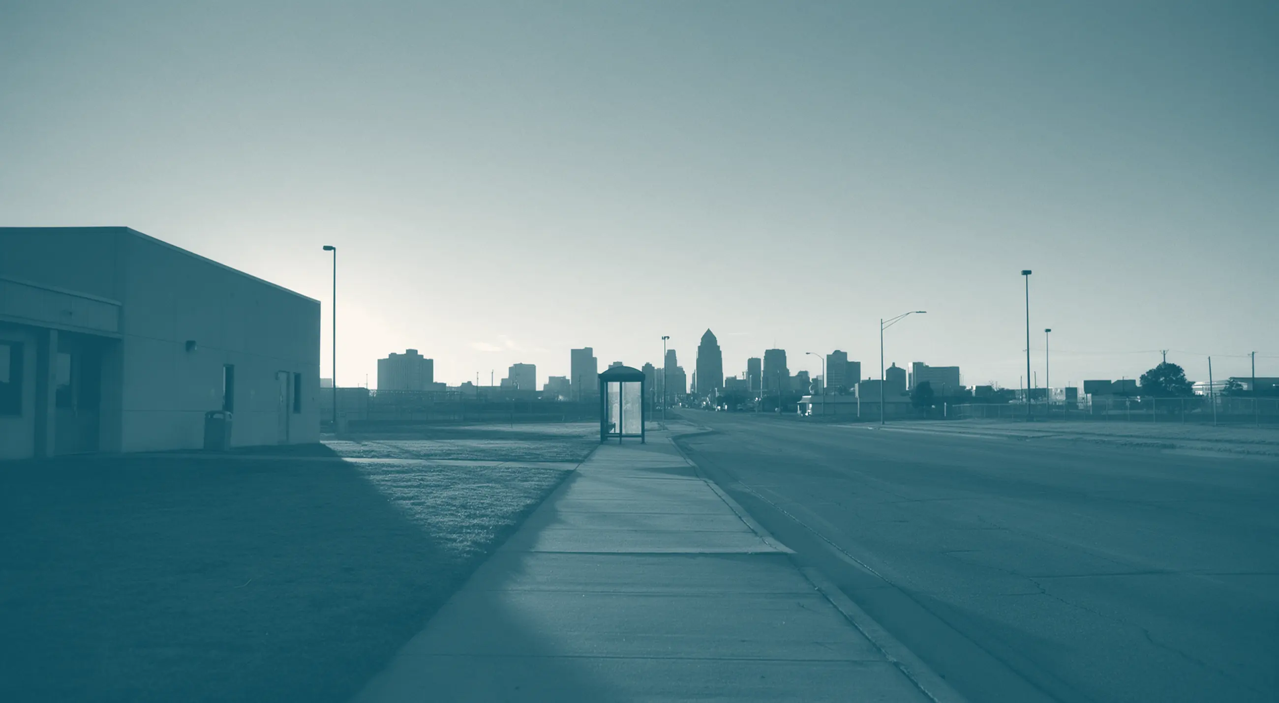 A sidewalk leading from a building toward a city at dawn.